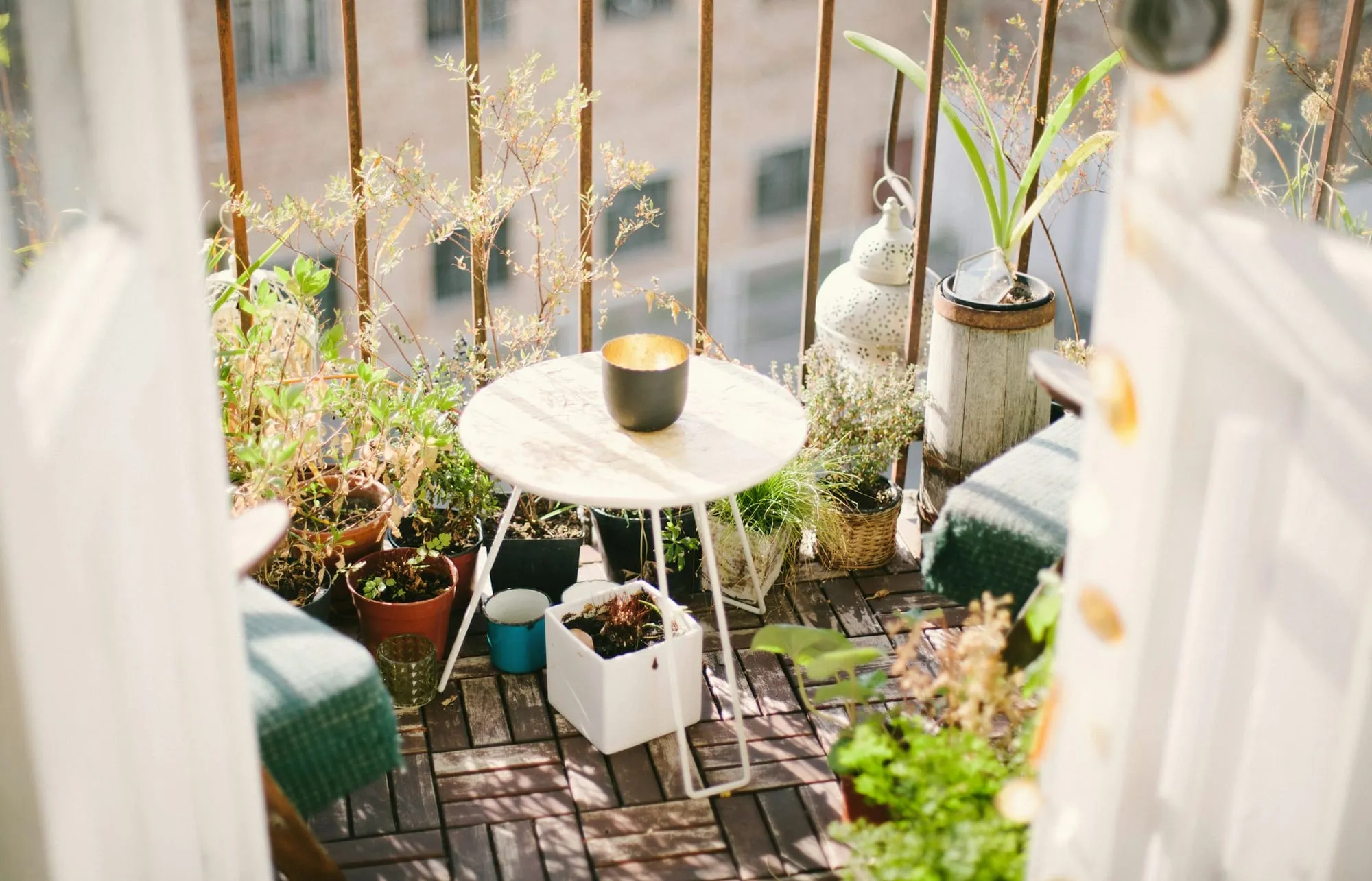 Kleiner Balkon mit Pflanzen und Tischchen, dahinter Nachbarhäuser